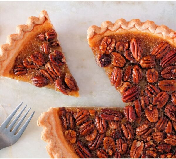 A partially sliced pecan pie with a rich filling is shown, topped with pecans; a fork sits on the plate beside the pie.