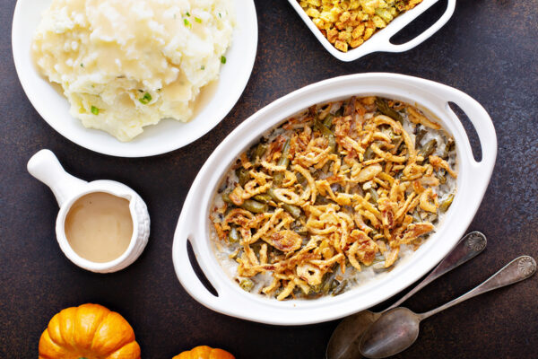 A Thanksgiving meal with green bean casserole, mashed potatoes, gravy, stuffing, and pumpkins decorating the table.