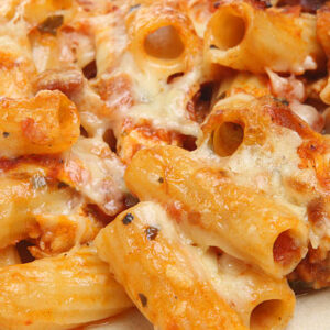 Close-up of baked rigatoni topped with melted cheese, rich tomato sauce, and sprinkled herbs.