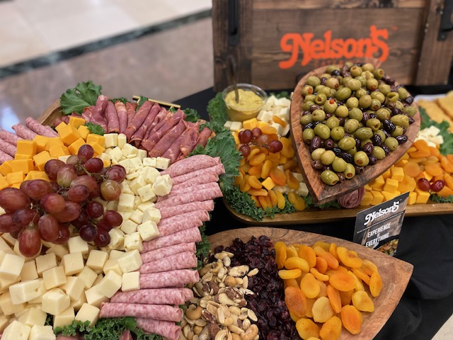 Charcuterie board with meats, cheeses, grapes, olives, nuts, dried fruits, mustard dip; wooden sign reads "Nelson's.