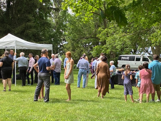 Crowd enjoying an outdoor park event with a white tent and food truck seen in the background.